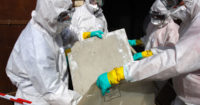 Workers in hazmat suits containing exposure